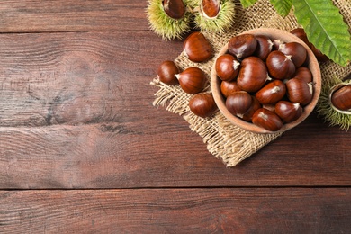 Fresh sweet edible chestnuts on brown wooden table, flat lay. Space for text