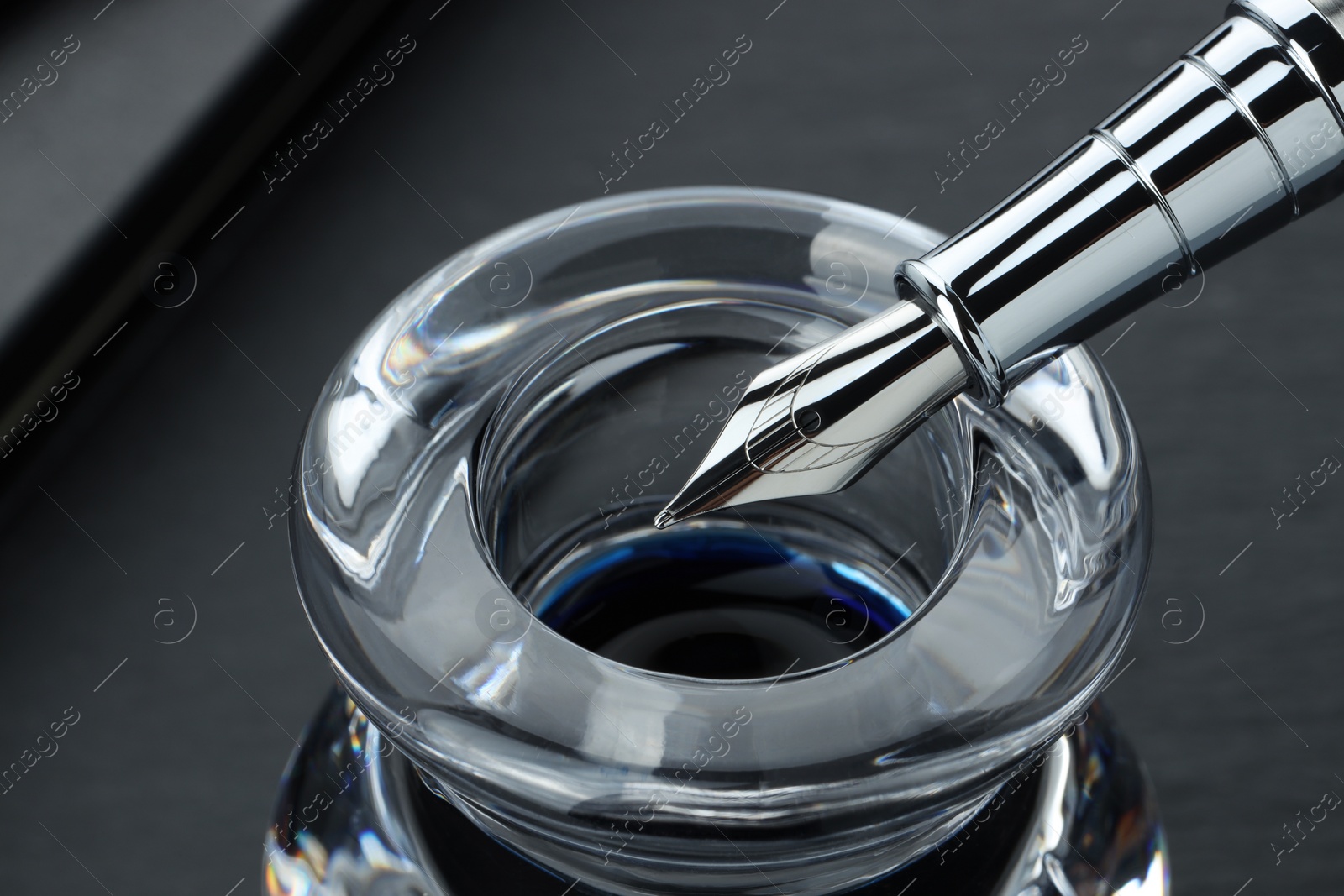 Photo of Inkwell with fountain pen on grey table, closeup