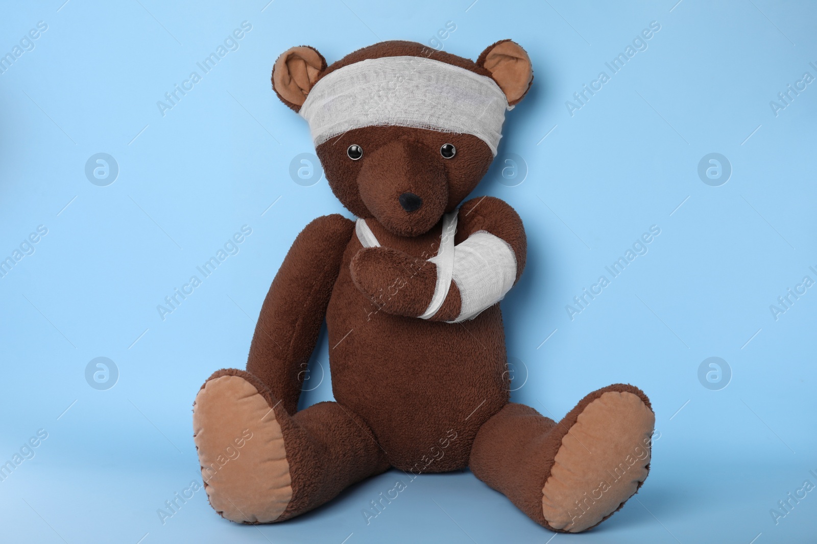 Photo of Toy bear with bandages on light blue background