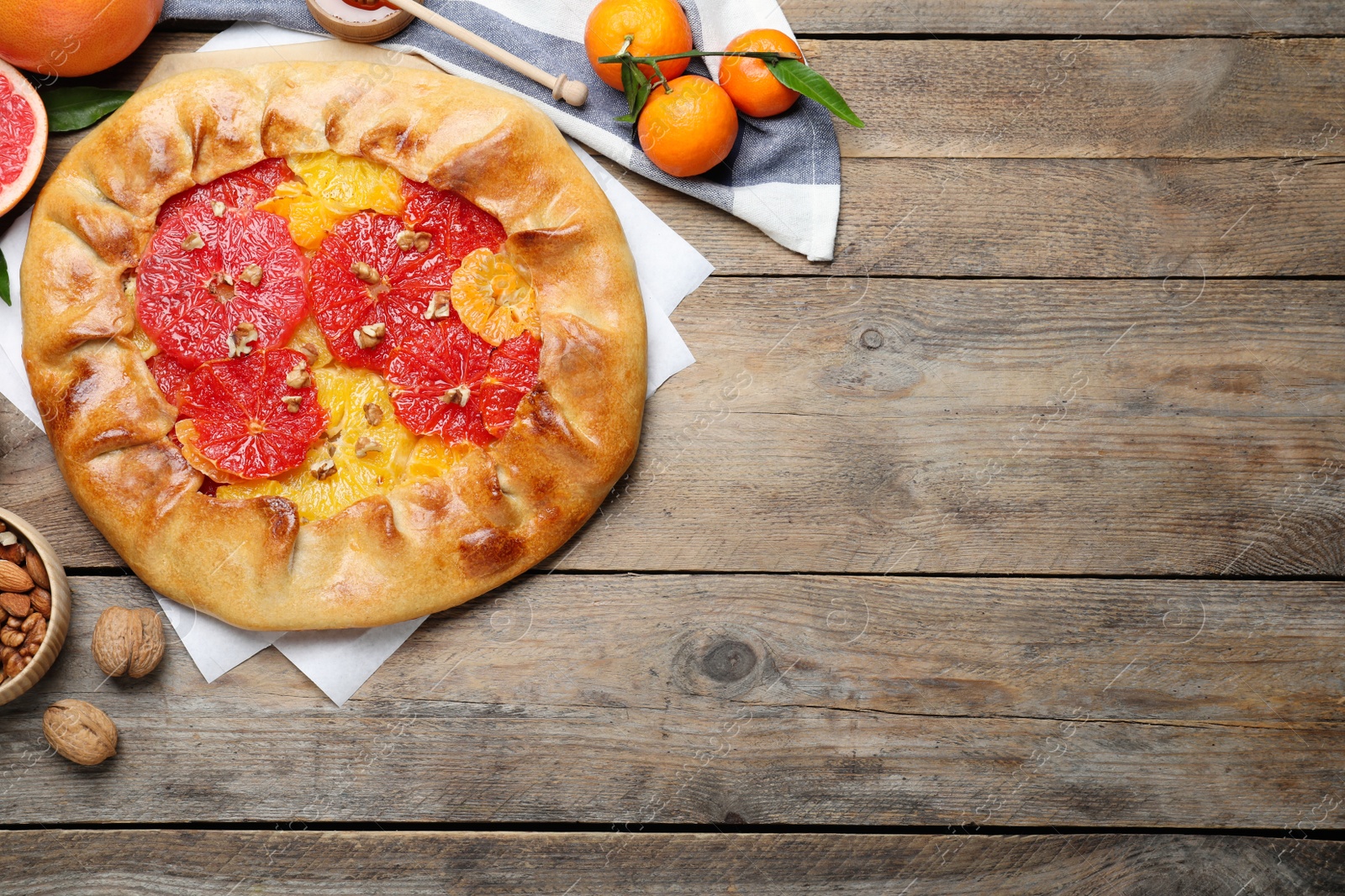 Photo of Delicious galette with citrus fruits and walnuts on wooden table, flat lay. Space for text