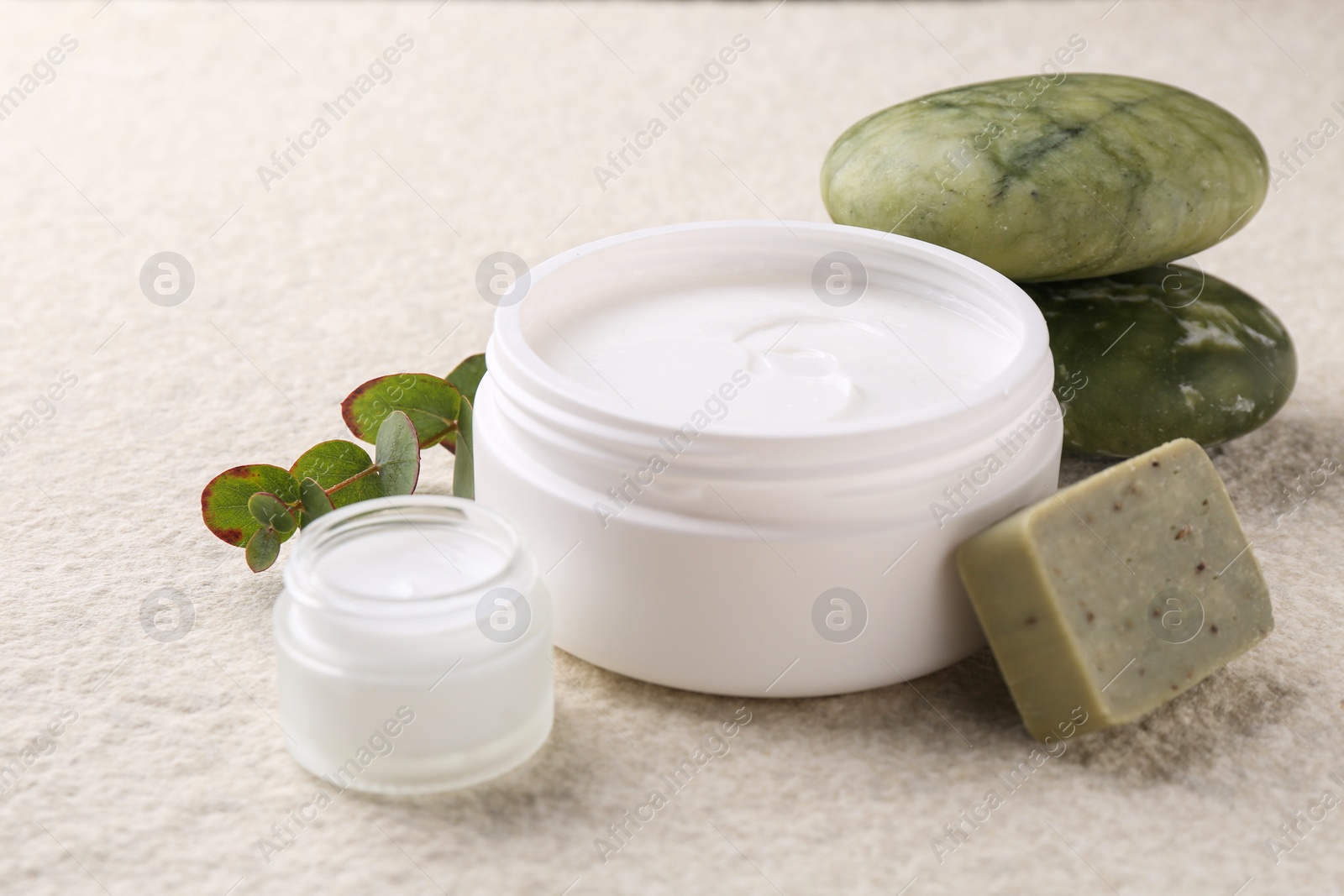 Photo of Composition with body care cream in open jars and soap bar on light textured table, closeup