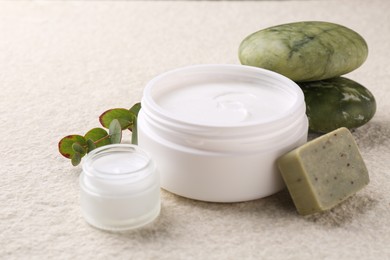 Photo of Composition with body care cream in open jars and soap bar on light textured table, closeup