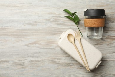 Lunch box, cutlery, glass cup and green plant on wooden background, flat lay with space for text. Conscious consumption
