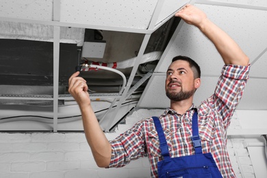 Photo of Professional technician repairing ceiling mounted air conditioner indoors