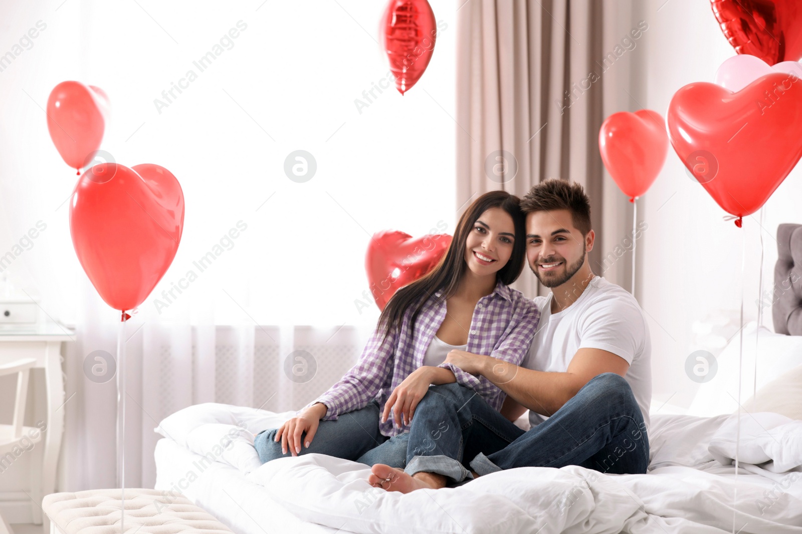 Photo of Lovely young couple in bedroom decorated with heart shaped balloons. Valentine's day celebration