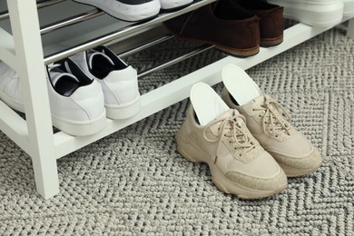 Photo of Orthopedic insoles in shoes on rug near rack, space for text