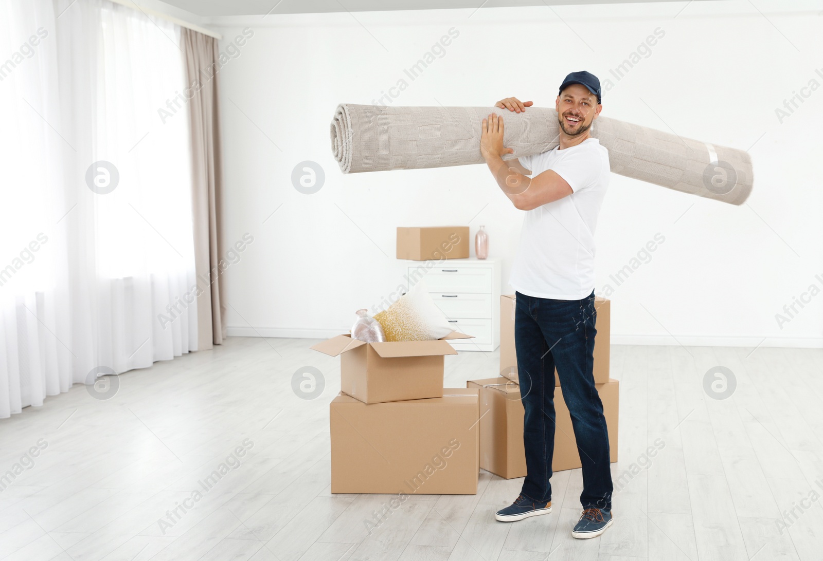 Photo of Moving service employees with cardboard boxes and carpet in room