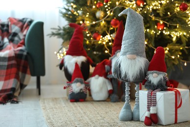 Photo of Funny Christmas gnomes with gift box on floor in room with festive decoration. Space for text