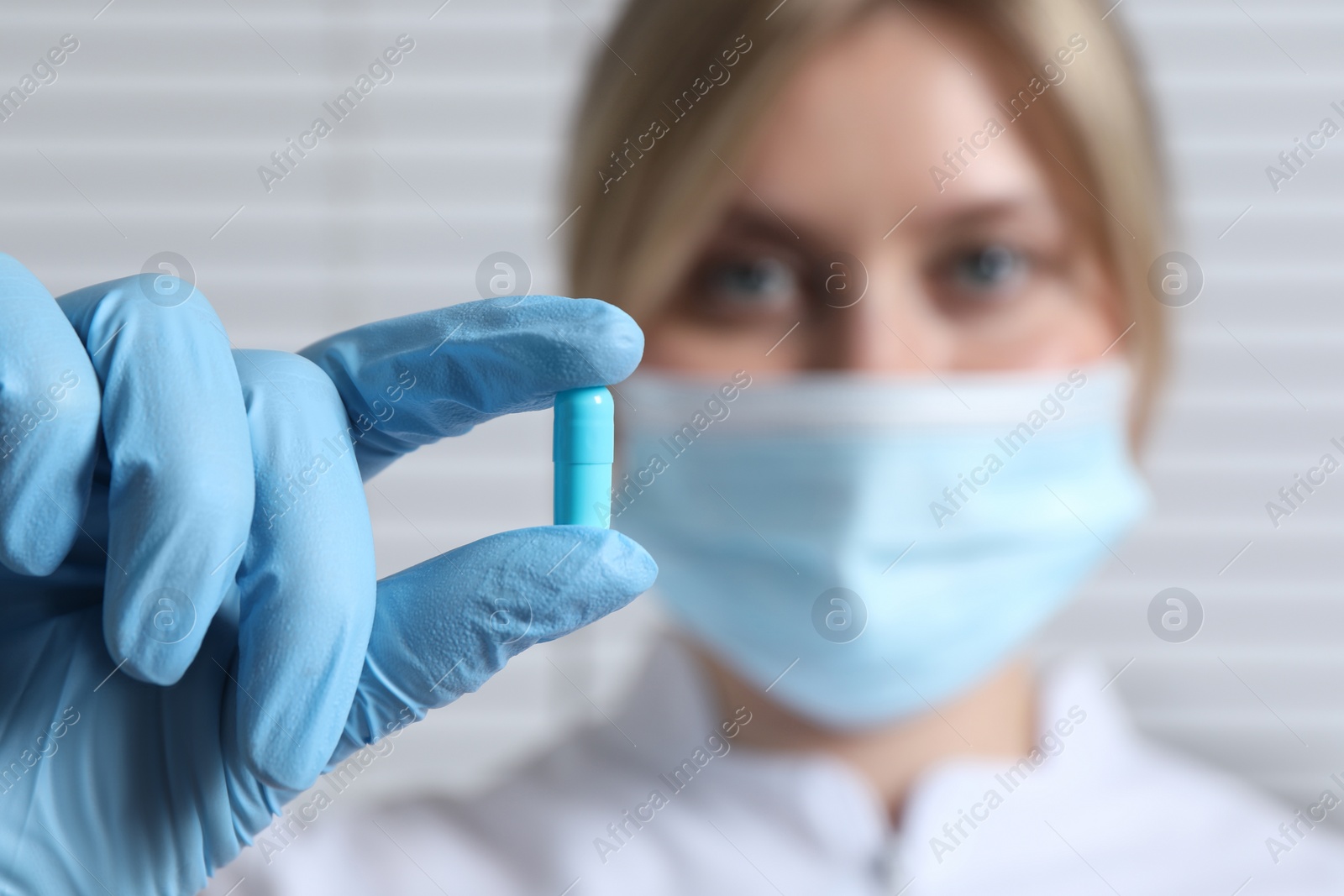 Photo of Doctor holding pill on light background, selective focus. Space for text