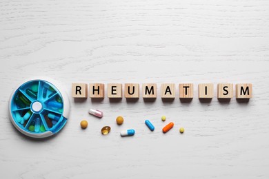 Photo of Word Rheumatism made of cubes and pills on white wooden table, flat lay