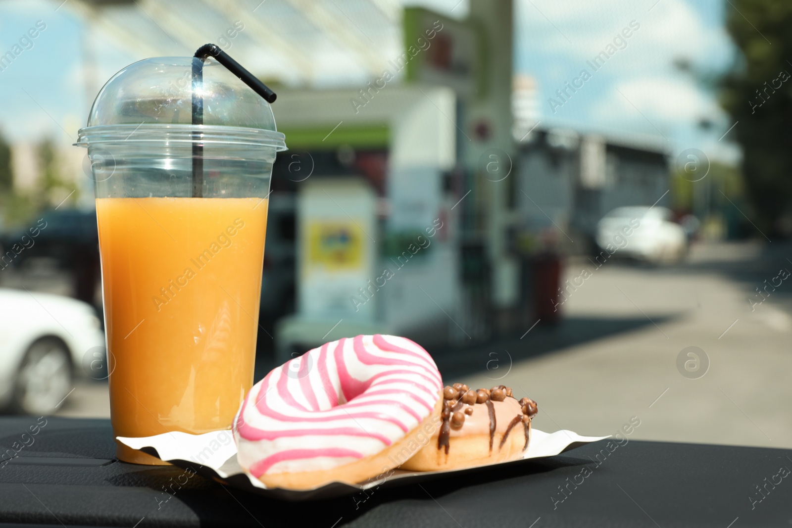 Photo of Plastic cup of juice and doughnuts on car dashboard at gas station. Space for text