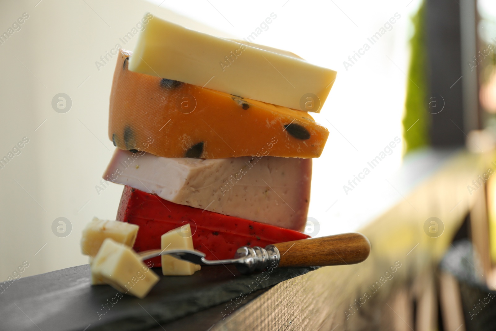 Photo of Different types of delicious cheeses and fork on wooden railing outdoors, closeup