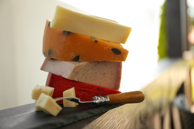 Photo of Different types of delicious cheeses and fork on wooden railing outdoors, closeup