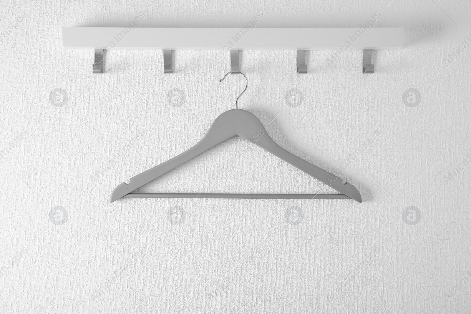 Photo of Rack with empty clothes hanger on light wall. Wardrobe accessory