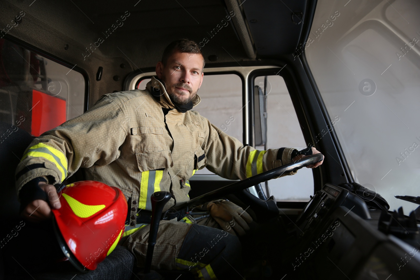 Photo of Firefighter in uniform with helmet driving modern fire truck