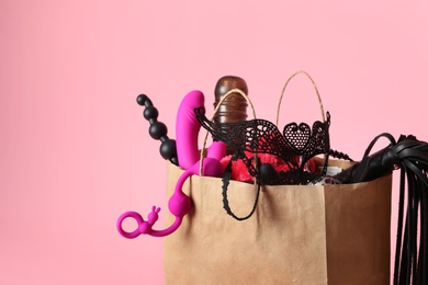 Photo of Paper shopping bag with different sex toys on pink background