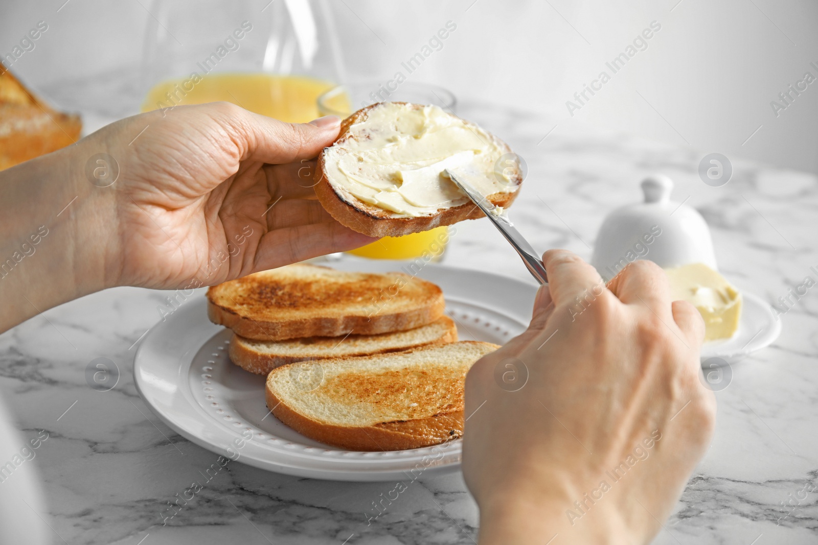 Photo of Woman spreading butter onto slice of bread over marble table, closeup