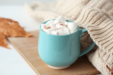 Cup of hot cozy drink with marshmallows and autumn sweater on table