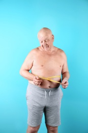 Photo of Fat senior man with measuring tape on color background. Weight loss