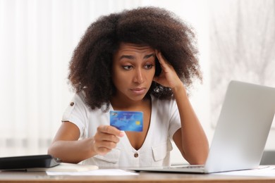 Photo of Confused woman with credit card and laptop planning budget indoors. Debt problem