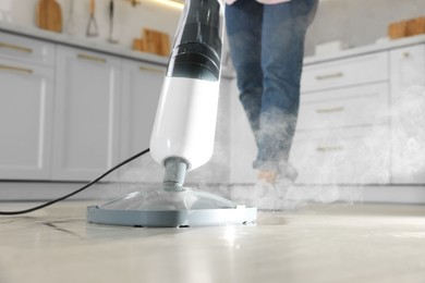 Photo of Woman cleaning floor with steam mop in kitchen at home, closeup
