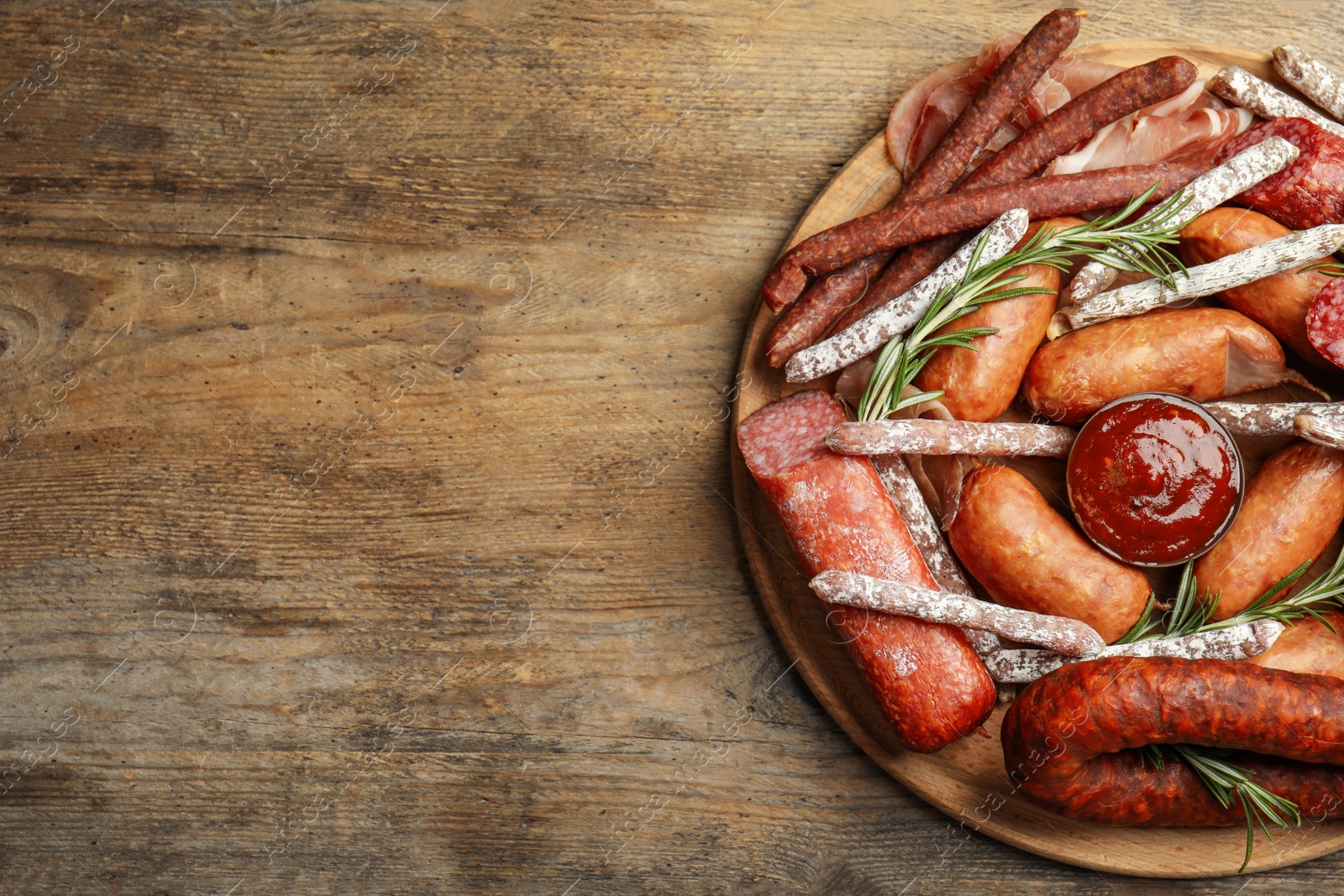 Photo of Different types of sausages with rosemary served on wooden table, top view. Space for text