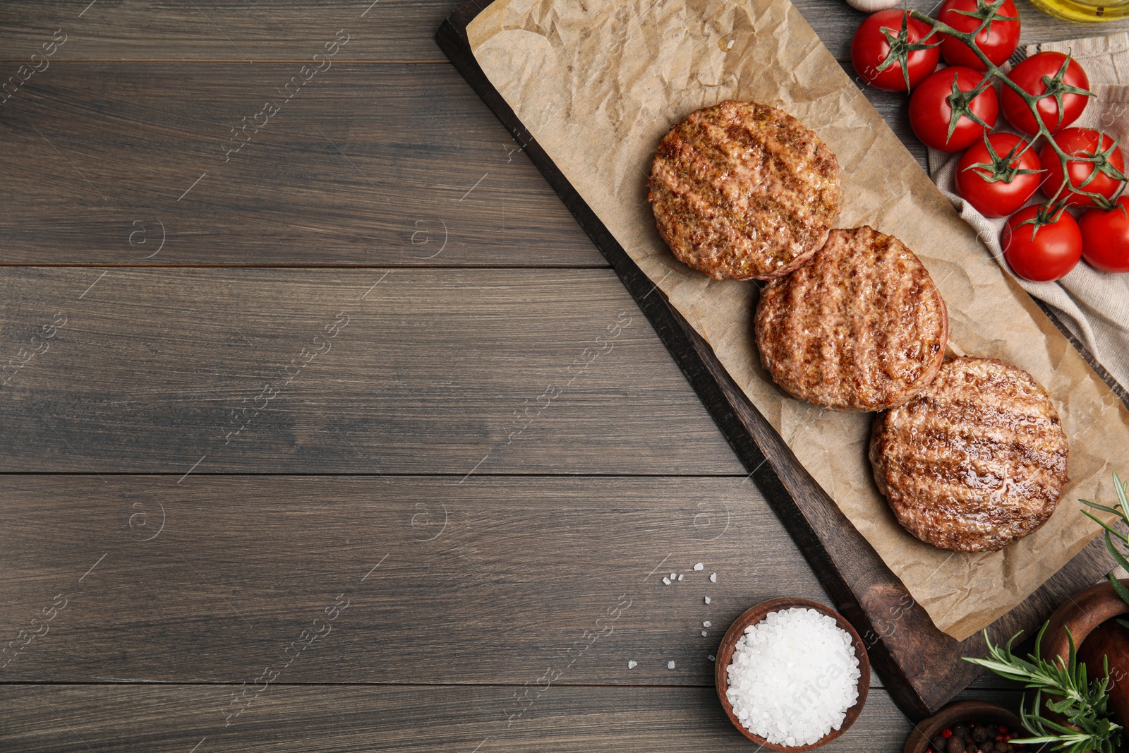 Photo of Board with tasty grilled hamburger patties and seasonings on wooden table, flat lay. Space for text