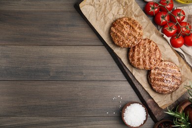 Photo of Board with tasty grilled hamburger patties and seasonings on wooden table, flat lay. Space for text