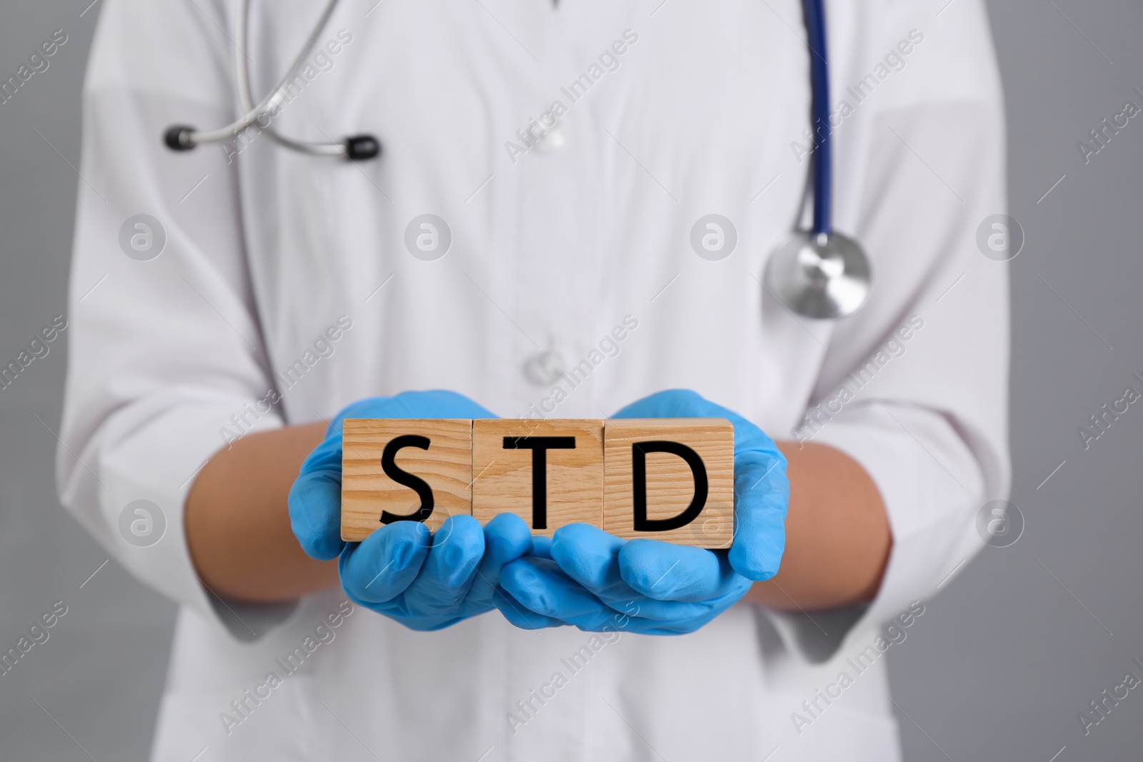 Photo of Doctor holding wooden cubes with abbreviation STD on grey background, closeup