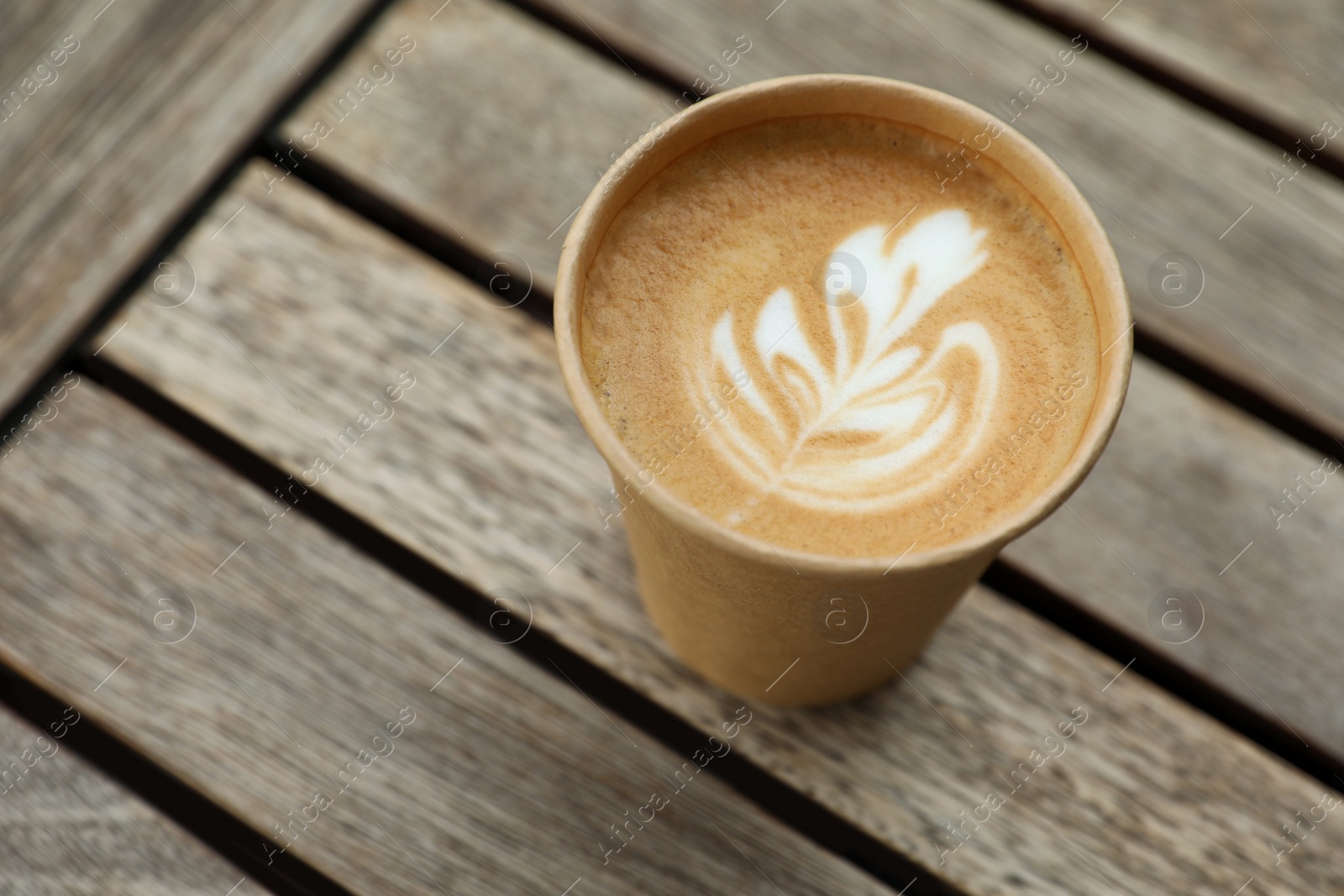 Photo of Takeaway paper cup with coffee on wooden table, above view. Space for text