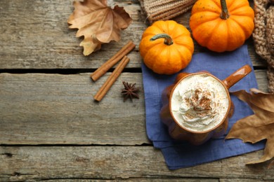 Mug of pumpkin spice latte with whipped cream, ingredients and dry leaves on wooden table, flat lay. Space for text