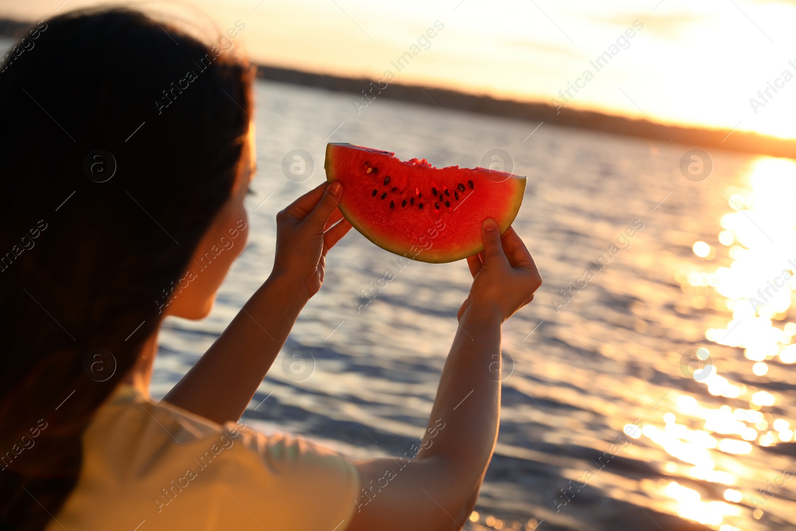 Photo of Young woman with watermelon near river at sunset, closeup