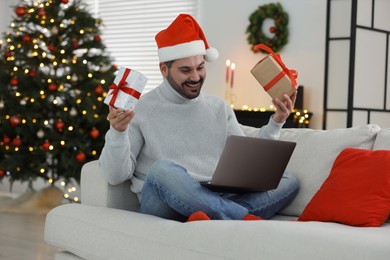 Celebrating Christmas online with exchanged by mail presents. Happy man with gift boxes during video call on laptop at home