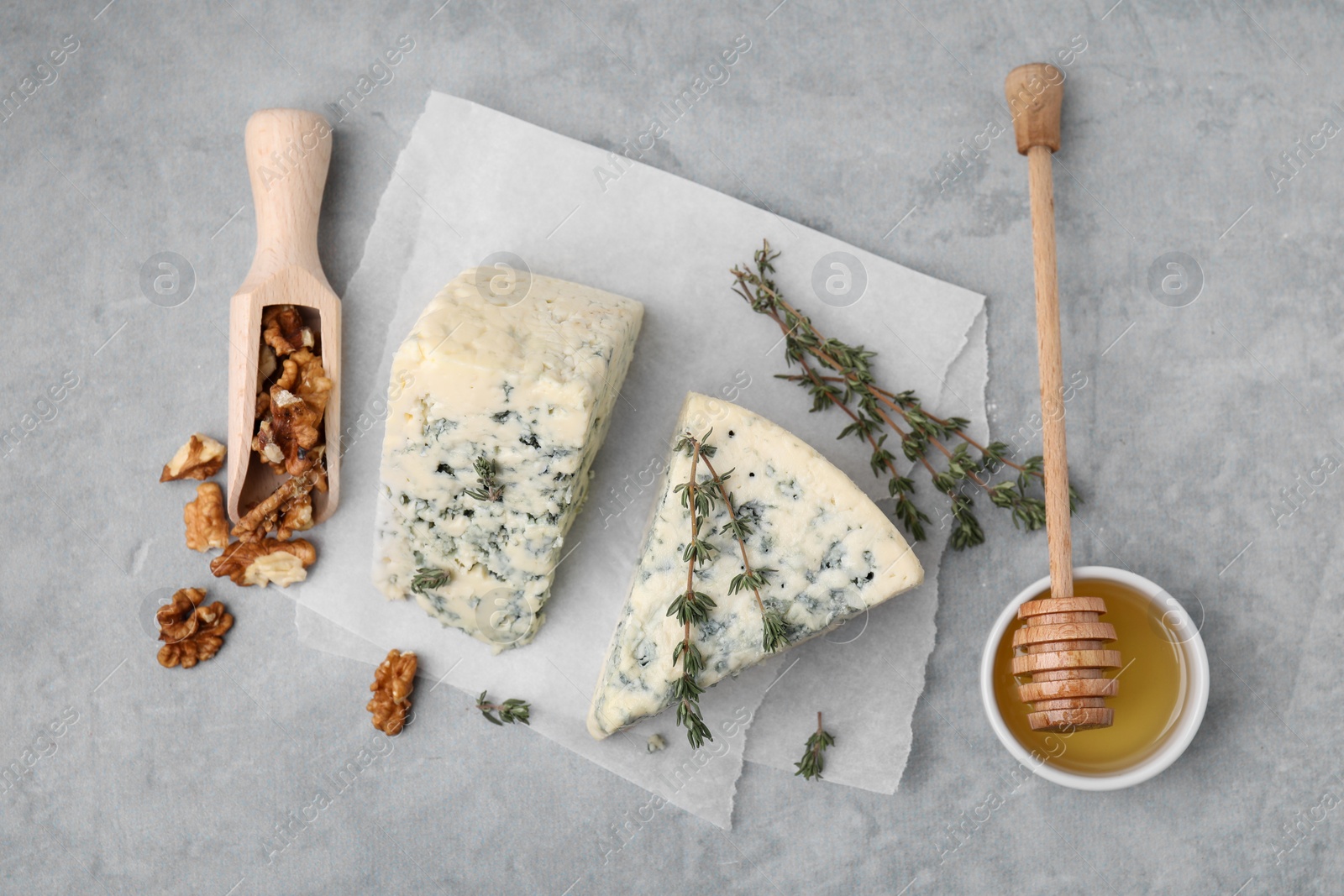 Photo of Tasty blue cheese with thyme, honey and walnuts on grey table, flat lay