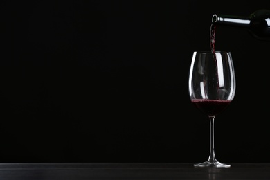 Photo of Pouring wine from bottle into glass on table against black background, space for text