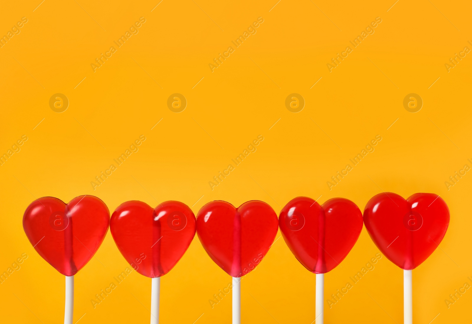 Photo of Sweet heart shaped lollipops on orange background, closeup view with space for text. Valentine's day celebration