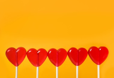 Sweet heart shaped lollipops on orange background, closeup view with space for text. Valentine's day celebration