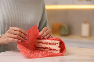 Photo of Woman packing sandwich into beeswax food wrap at light table in kitchen, closeup. Space for text