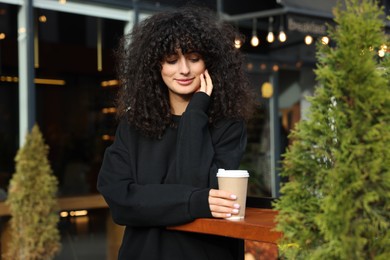 Photo of Young woman in stylish black sweater with cup of coffee at wooden table outdoors