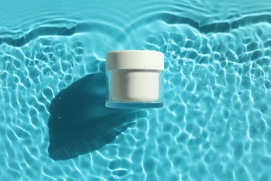 Photo of Jar with moisturizing cream in water on light blue background, top view