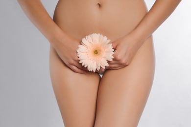 Photo of Young woman with flower showing smooth skin after bikini epilation on white background