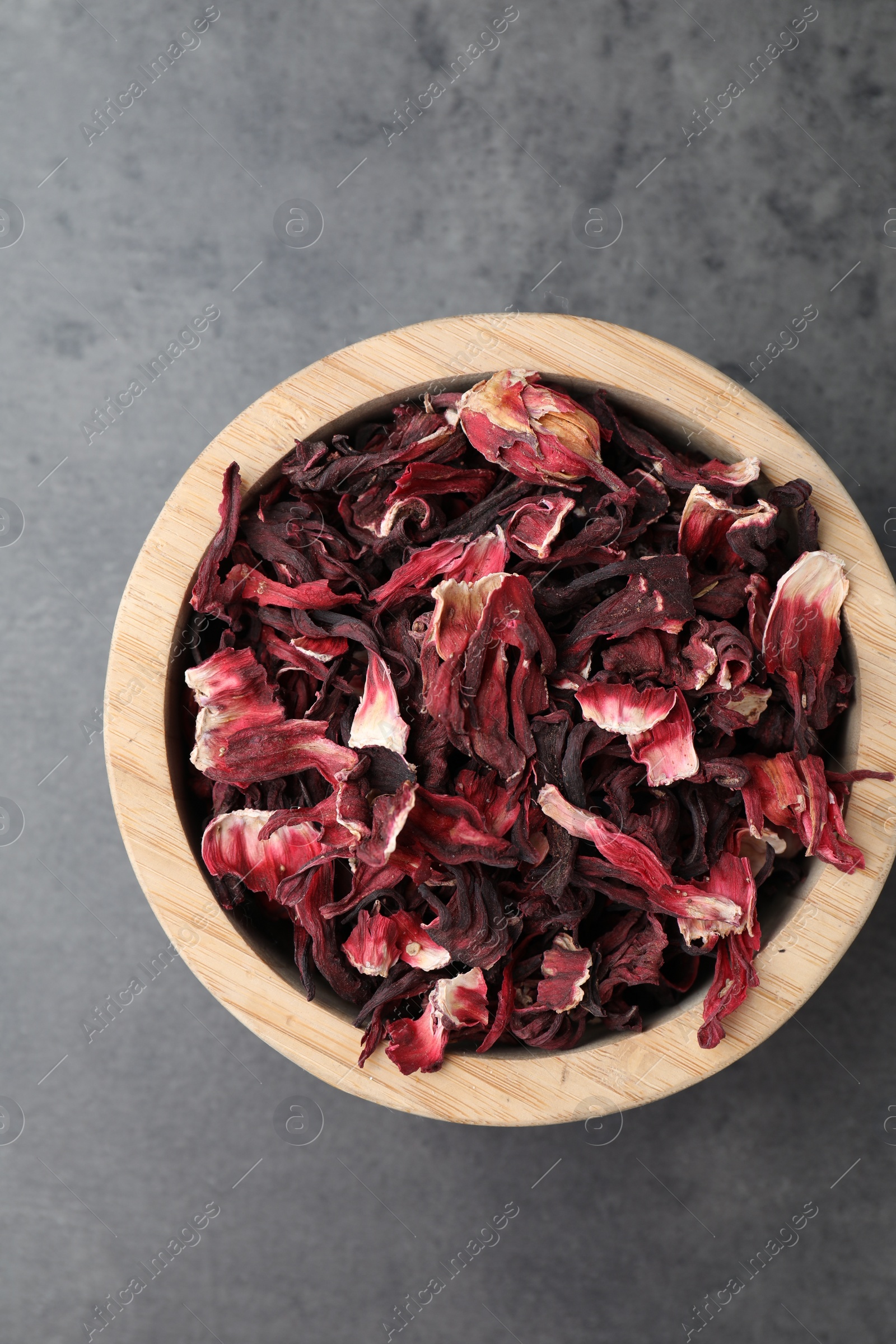 Photo of Hibiscus tea. Wooden bowl with dried roselle calyces on grey table, top view