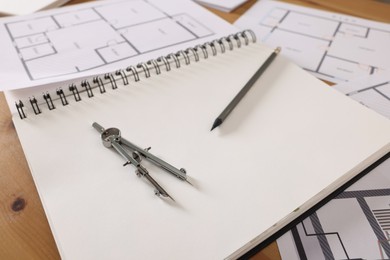 Photo of Sketchbook with construction drawings, pair of compasses and pencil on wooden table, closeup