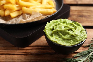 Photo of French fries, avocado dip and rosemary served on wooden table, closeup