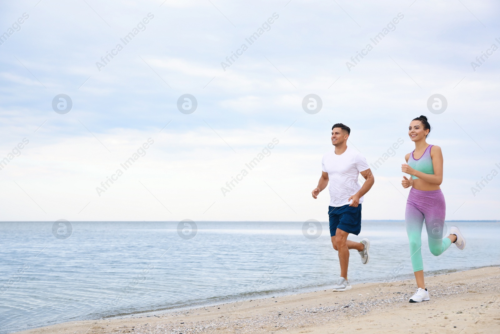 Photo of Couple running together on beach, space for text. Body training