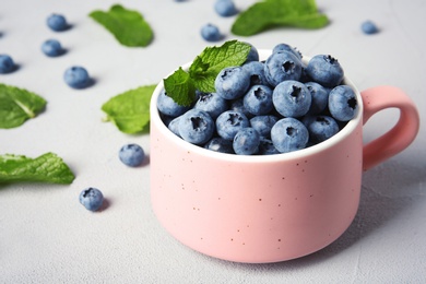 Photo of Cup with juicy blueberries and green leaves on color table