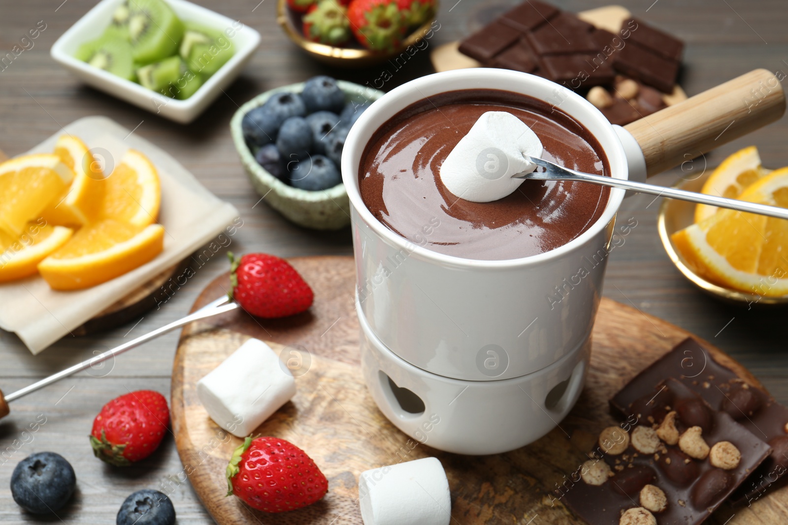 Photo of Dipping sweet marshmallow in fondue pot with melted chocolate at wooden table