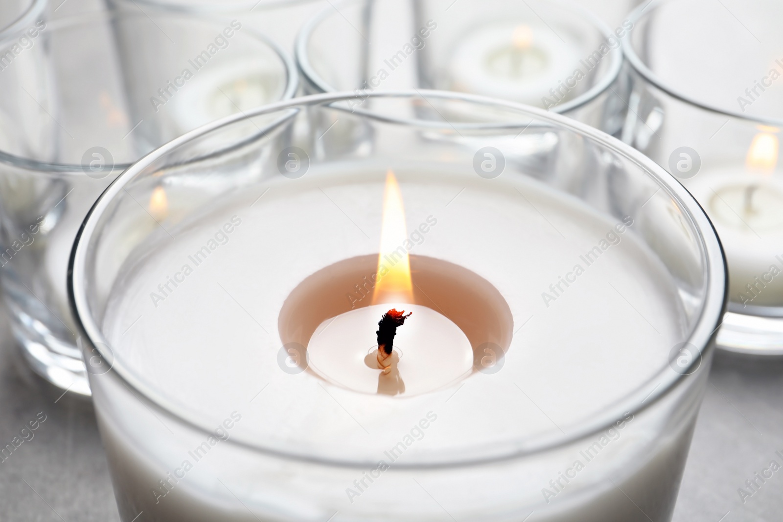 Photo of Burning wax candle in glass on table, closeup