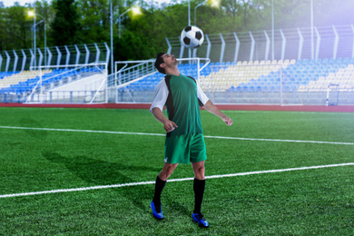 Image of Young man in uniform playing football at stadium