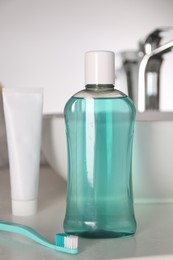 Photo of Bottle of mouthwash, toothpaste and toothbrush on light countertop in bathroom